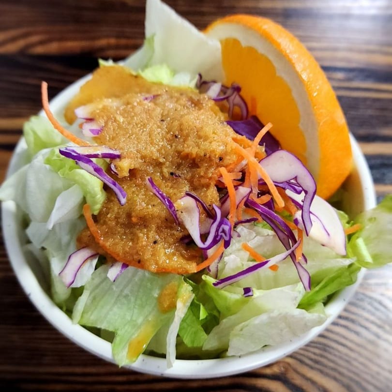 A fresh Akita Japanese Restaurant salad with lettuce, shredded carrots, red cabbage, and orange slice.