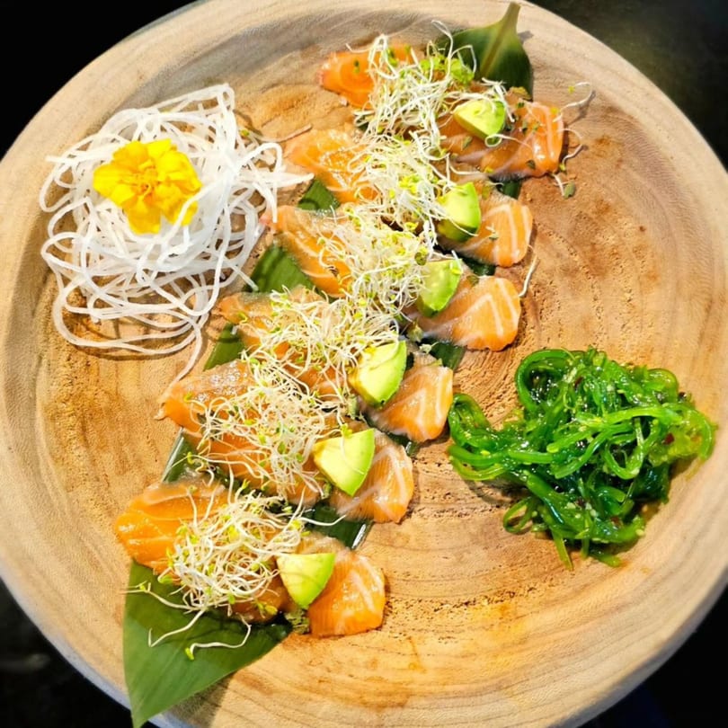 Akita Japanese Restaurant's salmon sashimi with avocado, sprouts, seaweed salad, and daikon on a wooden plate.